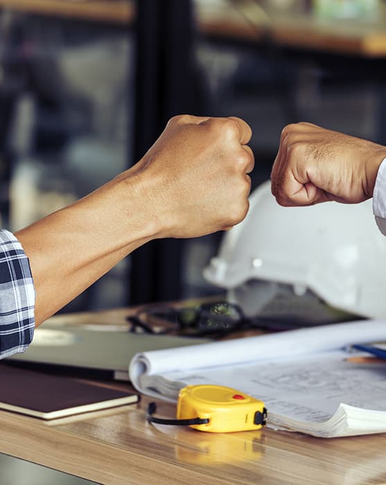 Two hands doing a fist bump above job paperwork and tools