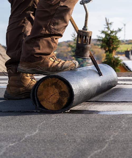A roofer using a torch and bitumen works on a commercial roofing installation job