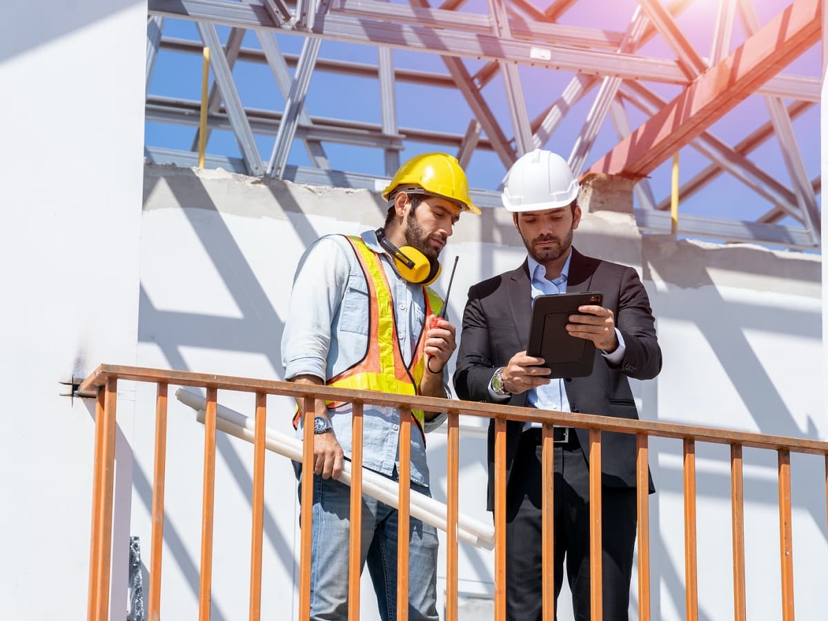 Two men in hard hats and safety vests focused on a laptop screen.