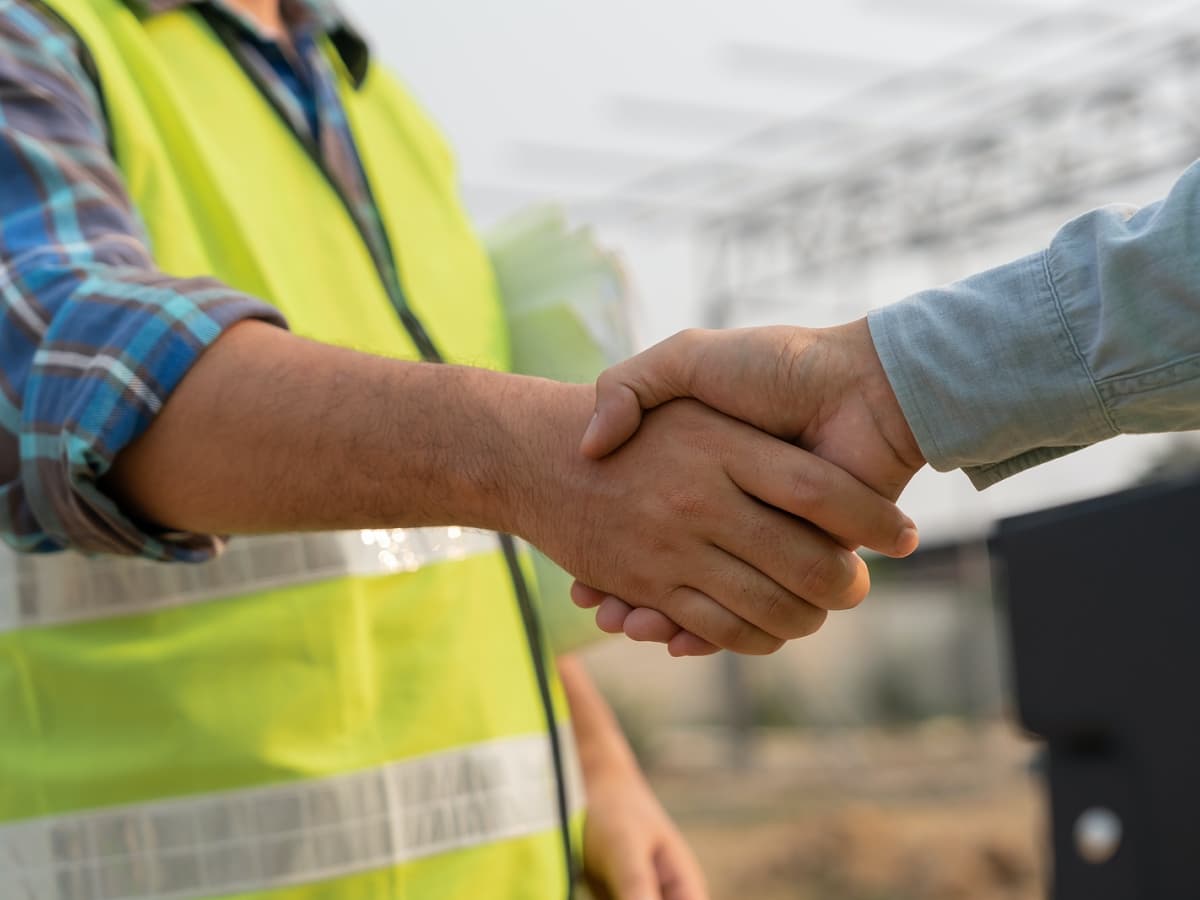 Two men shaking hands in front of a construction site, symbolizing a successful partnership in the construction industry.