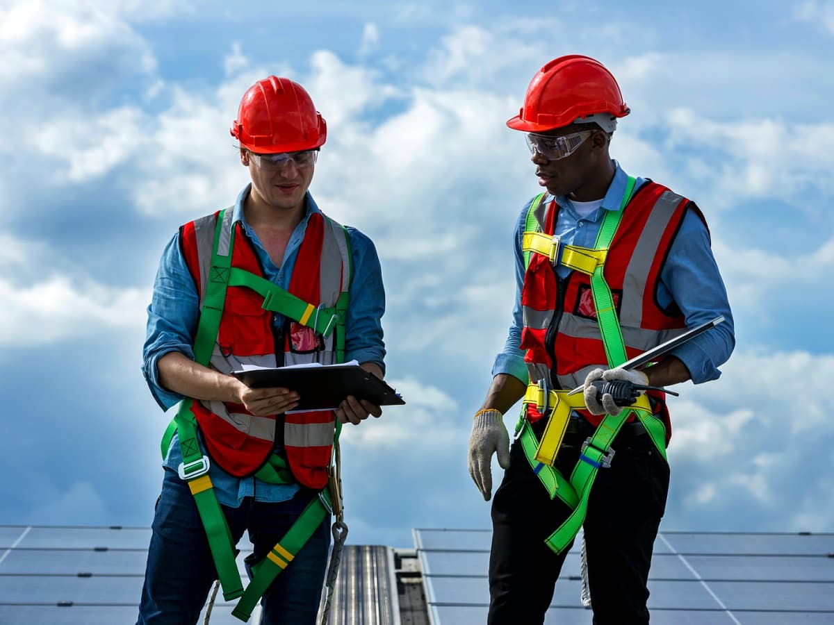 Two men in safety gear standing on a roof.