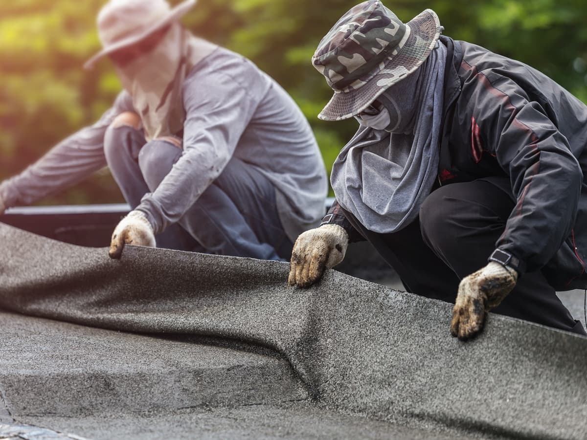Two workers in protective gear repairing a roof.